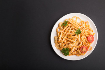 Semolina pasta with tomato pesto sauce, orange and herbs on a black background. Top view, copy space.