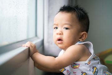 Happy baby boy stand near window looking to rainy outside