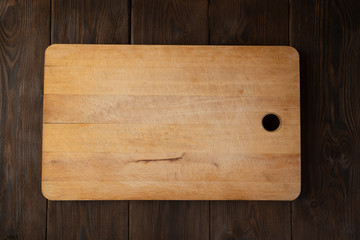 Wooden cutting Board on brown wooden background. The view from the top. Concept to create records, recipes, holiday compositions, birthday, Christmas.