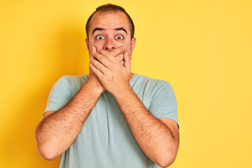 Naklejka premium Young man wearing green casual t-shirt standing over isolated yellow background shocked covering mouth with hands for mistake. Secret concept.