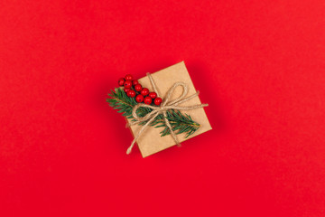 Craft gift box with spruce branch and red berries on red background. Holiday eco-friendly concept.