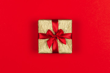 Golden gift box with red bow on the red background. Holiday concept.