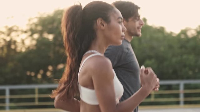 Side view of concentrated beautiful couple man and woman in sportswear running together while working out at playground outdoors
