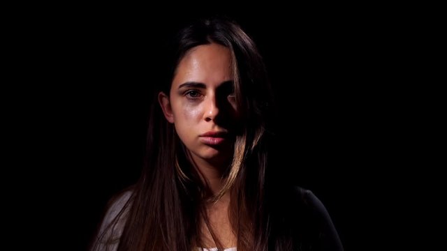 A tearful and frightened sad girl looking in the camera on black background. Domestic violence and social problems concept