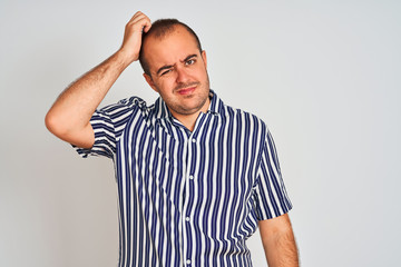 Young man wearing blue striped shirt standing over isolated white background confuse and wonder about question. Uncertain with doubt, thinking with hand on head. Pensive concept.