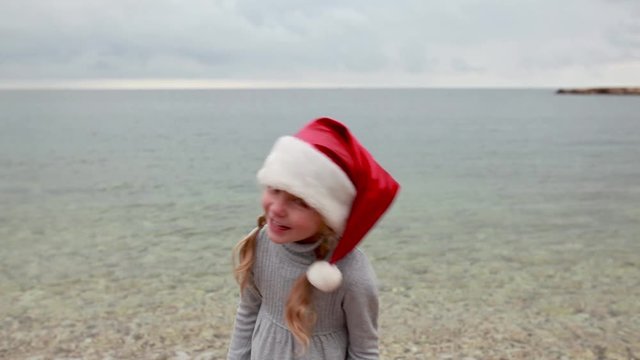 Little girl in santa hat plays on winter beach
