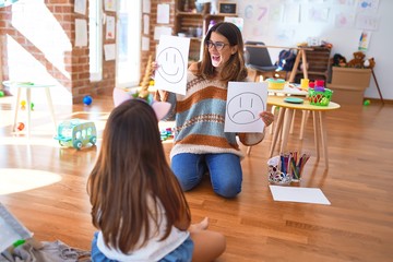 Beautiful pshychologist and toddler doing therapy with emotions emoji around lots of toys at kindergarten