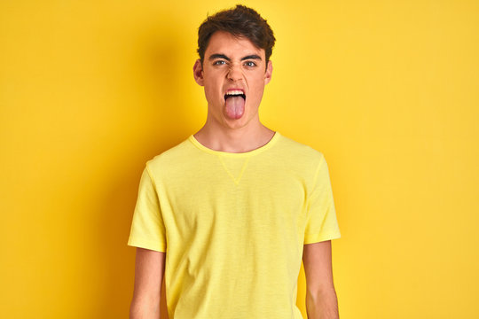 Teenager boy wearing yellow t-shirt over isolated background sticking tongue out happy with funny expression. Emotion concept.