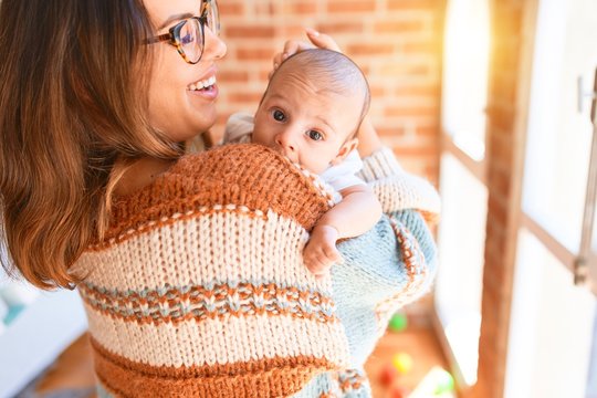 Young beautiful woman and her baby standing at home. Mother holding and hugging newborn