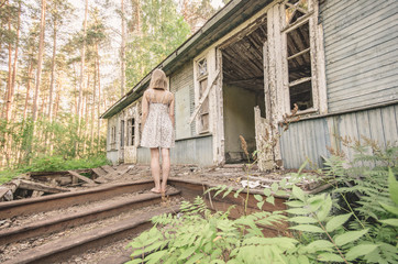 A woman in a dress stands in the background of an old abandoned dilapidated house