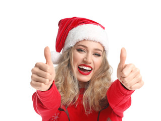 Beautiful young woman in Santa hat and Christmas clothes showing thumb-up gesture on white background