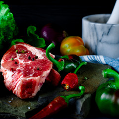 A set of raw products for the preparation of juicy meat steak with vegetables against a background of wild multicolored stone