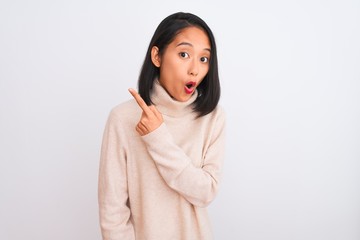 Young chinese woman wearing turtleneck sweater standing over isolated white background Surprised pointing with finger to the side, open mouth amazed expression.