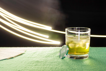 Glass misted glass with a drink and ice on the green table, the glare of light, drawing light. Poker chip next, dollars in the background