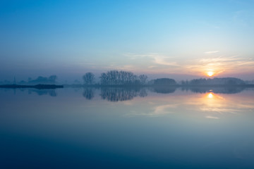Sunset on a foggy lake and trees on the horizon
