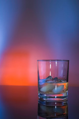 Glass whisky glass with ice in blue and orange light