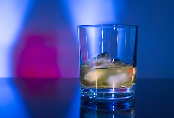 Glass whisky glass with ice in blue-pink light