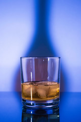 Glass whisky glass with ice in blue light
