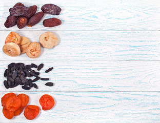 Heaps of dried fruits (fig, apricot, dates, raisins) on wooden background. Top view. Text space.