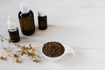 flax oil in dark glass bottles, flax seeds in a ceramic spoon and a sprig of flax