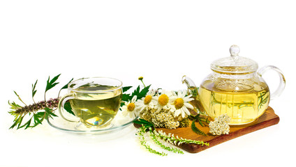 Herbal chamomile tea in a glass cup and teapot with fresh herbs(mother wort, chamomile, common yarrow) on cutting board isolated on white background