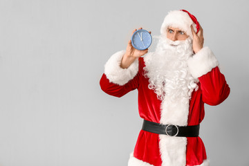 Confused Santa Claus with alarm clock on light background. Christmas countdown concept