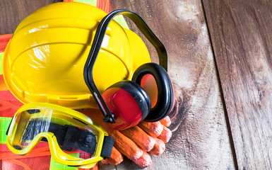 Standard construction safety equipment set on old wooden background including helmet, glasses, glove,  ear defenders and cloth. top view, safety first concepts