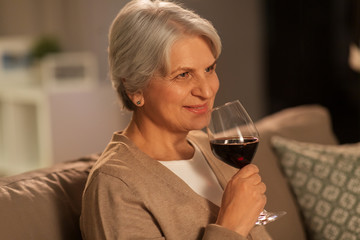 people, alcohol and drinks concept - happy smiling senior woman drinking red wine from glass at home in evening