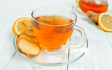 Glass cup of tea with ginger and lemon on a white wooden background.