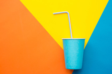 Blue paper cups with drinking colored plastic straws on beautiful multicolored background. Set for party. Top view. Minimalist Style. Copy, empty space for text