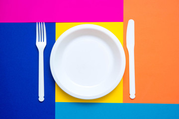 Plastic white fork, knife and plate on multicolored background. Cooking utensil. Top view. Minimalist Style. Copy, empty space for text