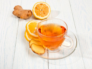 Glass cup of tea with ginger and lemon on a white wooden background.