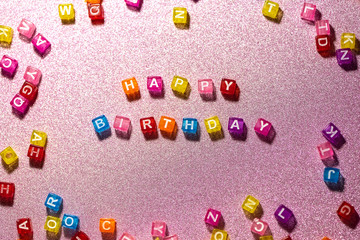 Happy Birthday with colored blocks letters on pink glitter backgrounds. Postcard to celebrate.
