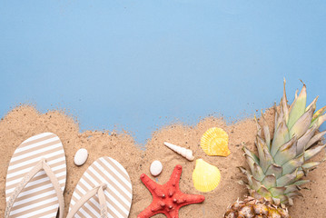Summer sea vacation background with copy space. Pineapple, starfish and flip flops on the sand over...