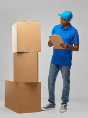 mail service and shipment concept - happy indian delivery man with boxes and clipboard in blue...
