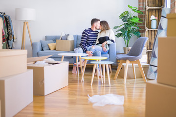 Young beautiful couple sitting on the sofa drinking cup of coffee and kissing at new home around cardboard boxes