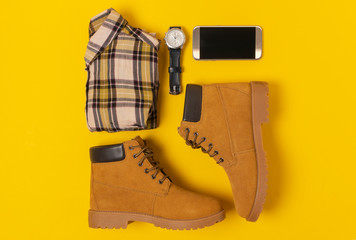 layout of autumn clothes and accessories in warm colors on a yellow background. Jeans, shirt, boots, phone and watch flat lay nearby