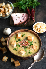 Pea soup with bacon, herbs and bread crumbs in rustic bowl on a dark background.