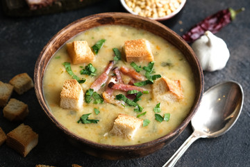 Pea soup with bacon, herbs and bread crumbs in rustic bowl on a dark background.