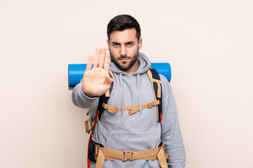 Young mountaineer man with a big backpack over isolated background making stop gesture with her hand