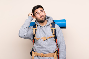 Young mountaineer man with a big backpack over isolated background having doubts and with confuse face expression