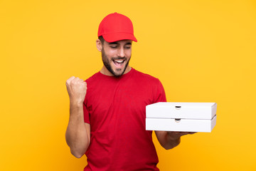 pizza delivery man with work uniform picking up pizza boxes over isolated yellow background celebrating a victory