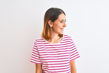 Fototapeta premium Beautiful redhead woman wearing casual striped pink t-shirt over isolated background looking away to side with smile on face, natural expression. Laughing confident.