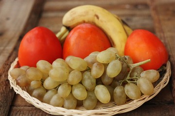 Persimmons bananas and grapes in a wooden basket 