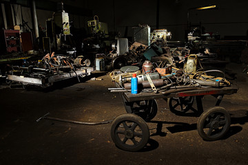 A dirty iron cart for manual movement stands in a dark workshop with tools. Dark cluttered workshop.