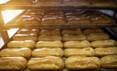 Many custard eclair cakes with butter cream and condensed milk lie on racks in the confectionery industry. Making desserts and sweets on an industrial scale, industry, background