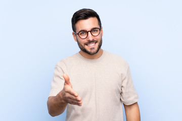 Young handsome man with beard over isolated blue background handshaking after good deal