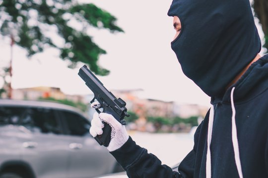 A terrorist man or thief or robber in black mask balaclava holding a gun.