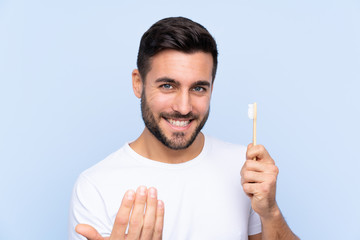 Young handsome man with beard brushing his teeth over isolated background inviting to come with hand. Happy that you came