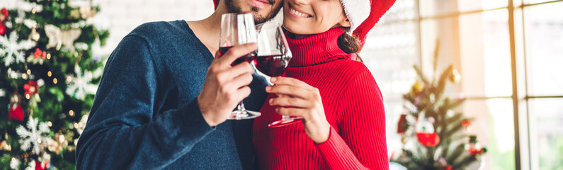 Romantic sweet couple in santa hats having fun and drinking wine glasses while celebrating new year eve and enjoying spending time together in christmas time at home